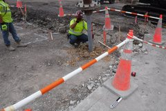 Man in yellow T-shirt and construction hat squatted in excavation dirt area