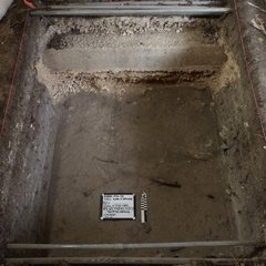 Square area inside an excavation unit with a small white board and ruler inside
