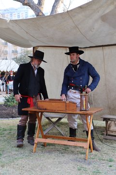 Two living historians standing by a wood table under a tented canopy