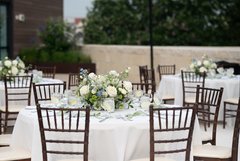 Three tables on a patio with white floral centerpieces and white linens