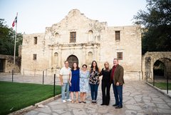 Six people in a row smiling in front of Alamo Church