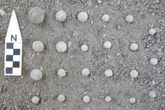Rows of small, round ammunition next a ruler pointing North on a bed of gravel