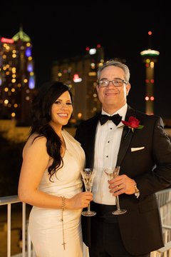 Bride and groom holding champagne glasses with view of downtown San Antonio at night behind them