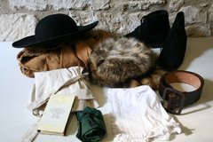Clothing inside history trunk including black hat, coonskin cap, black shoes, and belt