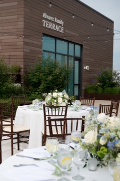 Tables set with white floral centerpieces and white linens on Alvarez Family Terrace with signage in the background