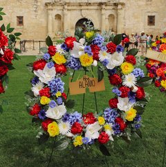 Red, white, blue, and yellow floral wreath in the lawn in front of Alamo Church