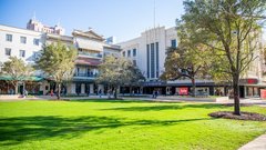 Large grass area in an outdoor community park bordered by a hotel and shops