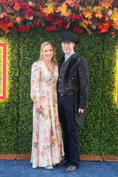Woman in long floral dress and man wearing a black cowboy hat and black clothes against a floral backdrop