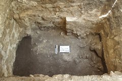 Inside of a rocky excavation unit with a dark clay area at the bottom