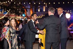 A group of guests wearing black tie attire under string lights outdoors at an event