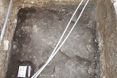 Inside of a rocky excavation unit with two white pipes diagonal across unit