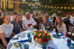Five smiling people seated at a round table with bright colorful florals in Alamo Gardens