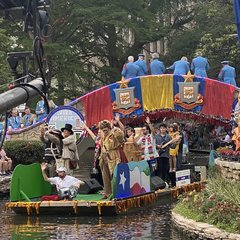 Commissioner Buckingham waving at the audience on a river parade float with a decorative large Alamo sculpture