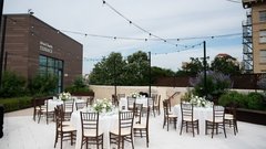 Tables set for an event with white floral centerpieces and white linens under string lights on a patio