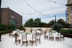 Tables set for an event with white floral centerpieces and white linens under string lights on a patio