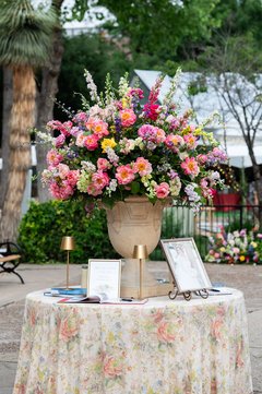 Large centerpiece of Spring flowers on a small round table with floral linens and a guestbook for signing