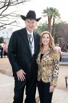 Tall man wearing a black cowboy hat and tuxedo with a bolo and a woman in a gold jacket and black pants