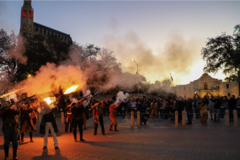 A crowd in front of Alamo Church watches living historians firing muskets on Alamo Street