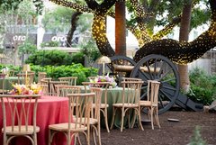 Round tables and rustic wood chairs set out by a demonstration cannon in Alamo Gardens