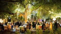 Guests seated at round tables at an event in the gardens with string lights in the trees