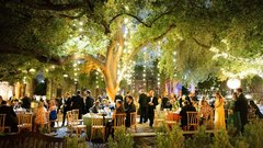 Guests seated at round tables at an event in the gardens with string lights in the trees