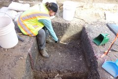 Archaeologist sitting outside of an excavation unit digging inside