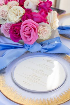 Round menu set inside charger next to colorful flowers and a blue napkin