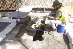 Archaeologist sitting on a blue bucket inside an excavation unit