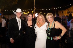 Man in white cowboy hat and black tuxedo with three woman, two dressed in black and one in a white dress