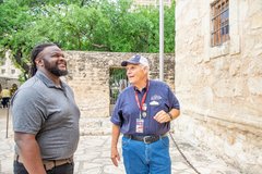 Visitor looking at Alamo Church wall while a volunteer speaks to him