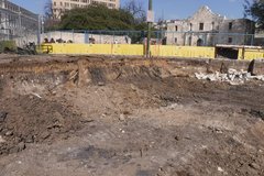 Dirt construction area with yellow water barriers and fencing to the left of Alamo Church