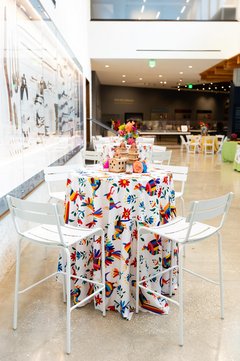 Cocktail tables with otomi linens and white chairs set up for an event inside a museum lobby