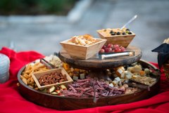 Two tiered wooden serving dish with nuts, meats, and cheese squares placed on a red linen
