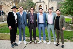 Six young men standing in a row, smiling at an outdoor event