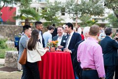 Guests enjoying an event, standing around a cocktail table with red linens and colorful flowers