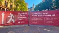 Red fence wrap noting pedestrians welcome and businesses open