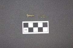Two small historic jewelry clasps on a gray background next to a ruler for size