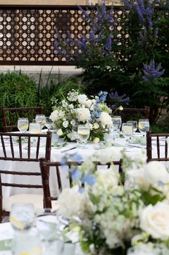 Tables with white floral centerpieces against an arbor on a patio