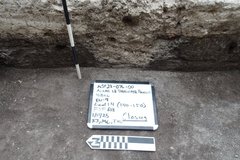 Posthole of rock with a white board on the surface and ruler for size