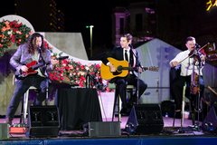 Three musicians on stage performing at event with floral parapet arch as backdrop
