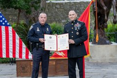 Marine General holding a certificate with an Officer in front of the American and Marines flags