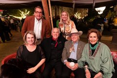 Four seated guests and two standing guests behind them in a tented area in Alamo Gardens