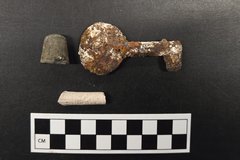 Thimble, key, and clay pipe stem artifacts next to a ruler for size