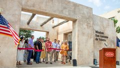 Opening to concrete gate closed off by a red ribbon with family members behind the ribbon