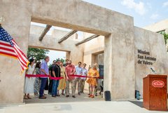 Opening to concrete gate closed off by a red ribbon with family members behind the ribbon