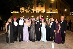 Wedding guests in black tie attire, some wearing bright cowboy hats, in Alamo Plaza at night