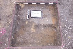 Inside of an excavation unit with a marker and white board with pink rope at the top perimeter