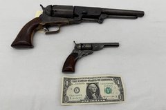 two revolver guns side by side with a dollar bill shown for size