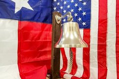 Bell against a Texas flag and a USA flag