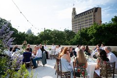 Guests seated at tables with white linens and string lights, Emily Morgan Hotel in the background